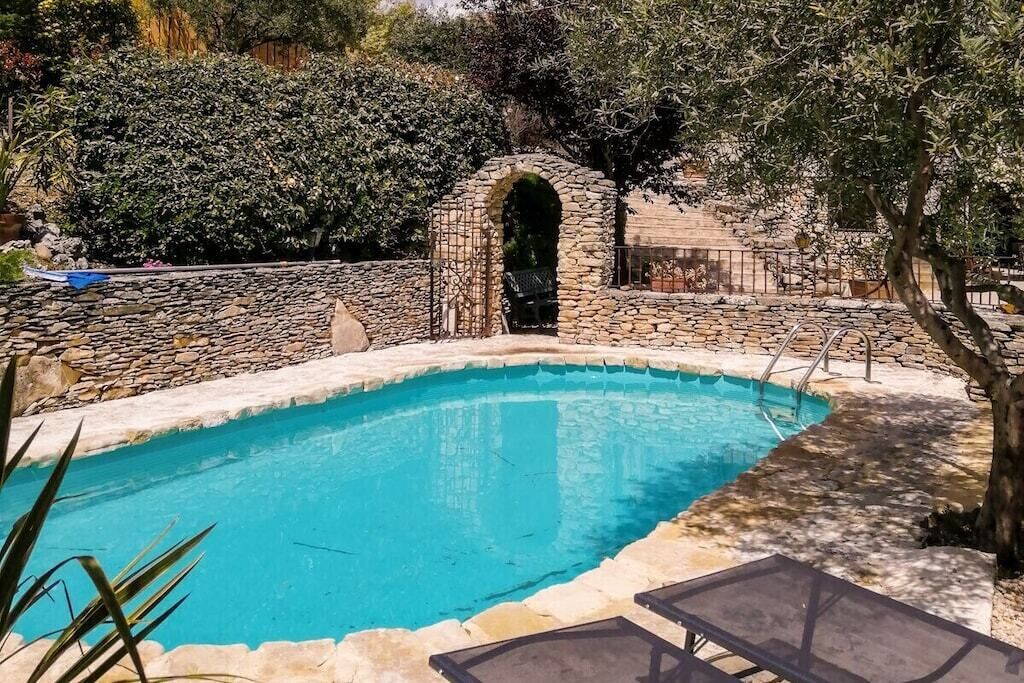 A swimming pool with a stone wall and an arched entrance, surrounded by trees and a stone fence.