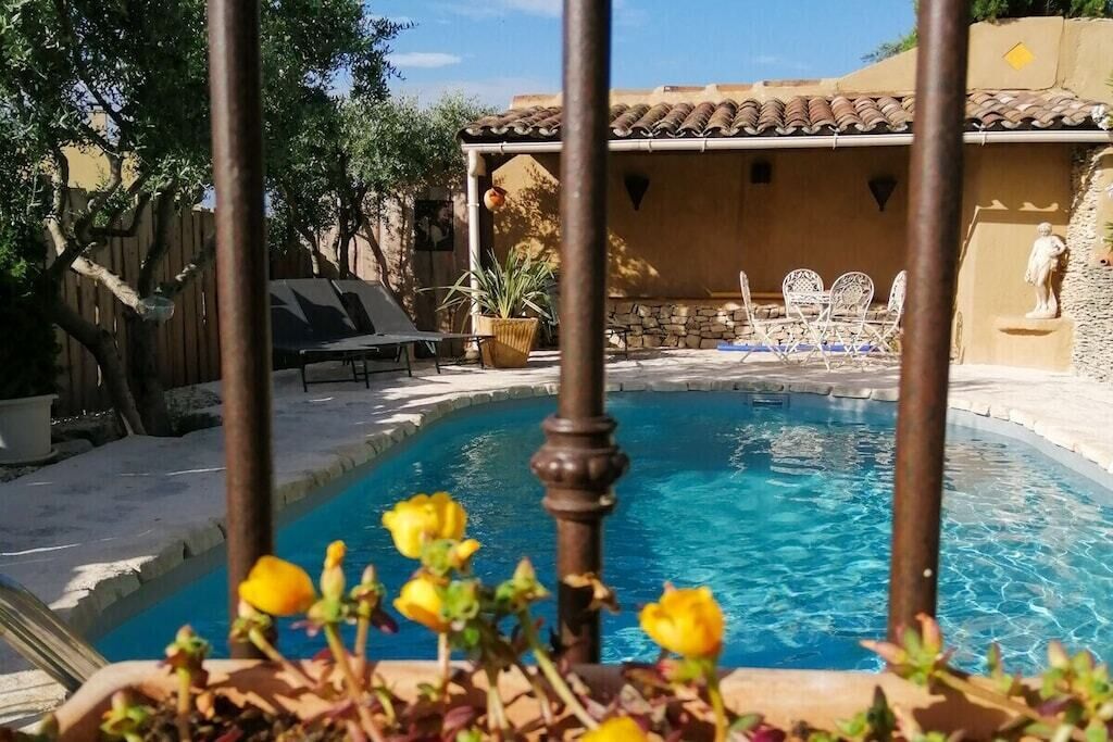 A swimming pool with a tiled deck, lounge chairs, and a stone wall with a statue.