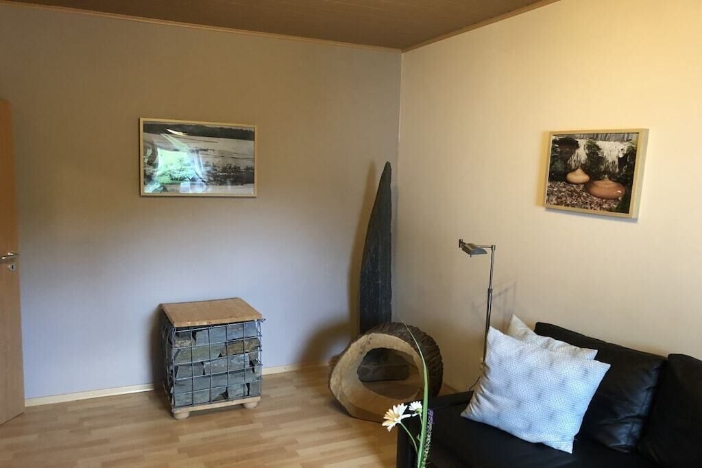 Une pièce avec un canapé en cuir noir, un meuble en bois, un panier pour animaux de compagnie et deux tableaux encadrés accrochés au mur.