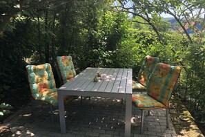 Eine Terrasse mit Tisch und vier Stühlen, umgeben von viel Grün.