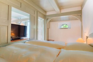 A room with a television on a wooden stand, a bed with white bedding, a small table, and a lamp. - Friesenhaus Sara (S4) (Wenningstedt)