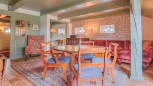 Uma sala de estar acolhedora com uma mesa de vidro redonda, cadeiras de madeira, um sofá estampado e um painel decorativo.