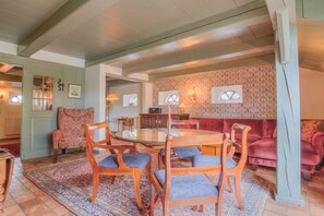 Una sala de estar acogedora con una mesa redonda de vidrio, sillas de madera, un sofá estampado y una pared decorativa.