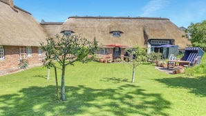 Uma casa com telhado de palha, um gramado bem cuidado e área de estar externa.