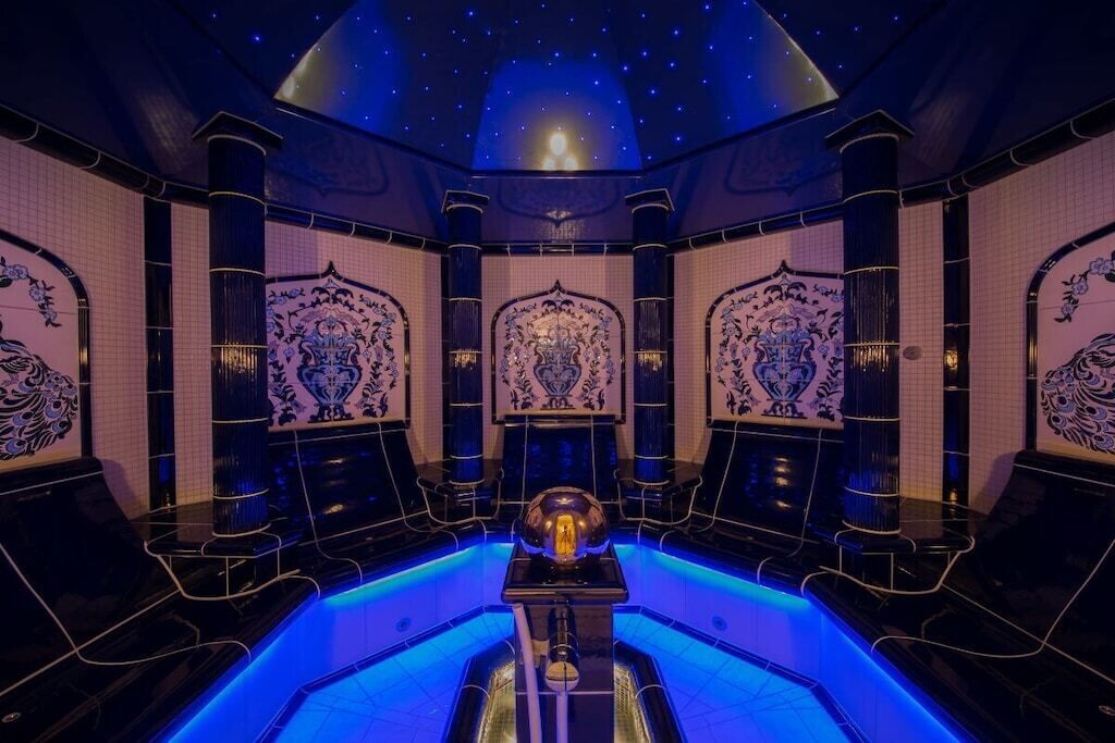 Une chambre luxueuse dotée d’une piscine centrale, de motifs décoratifs élaborés sur les murs et d’un plafond étoilé.