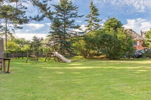 Une cour arrière avec une balançoire, un toboggan et une maison en briques en arrière-plan.