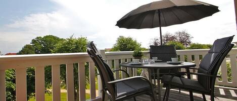 An outdoor patio with a table and chairs, a large umbrella, and a view of greenery.