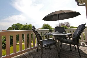 Eine Außenpatio mit Tisch und Stühlen, einem großen Sonnenschirm und Blick ins Grüne.