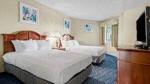 Ein Hotelzimmer mit zwei Betten, einem Schreibtisch, einem Fernseher und Kunstwerken an den Wänden.