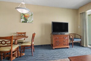 Ein Hotelzimmer mit Esstisch, Stühlen, einem Fernseher auf einer Holzkommode und einem Gemälde an der Wand.