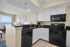 A modern kitchen with white cabinets, a black countertop, a built-in microwave, and a dishwasher. - Oceanfront 1BR Suite + Lazy River & Hot Tub (Myrtle Beach)