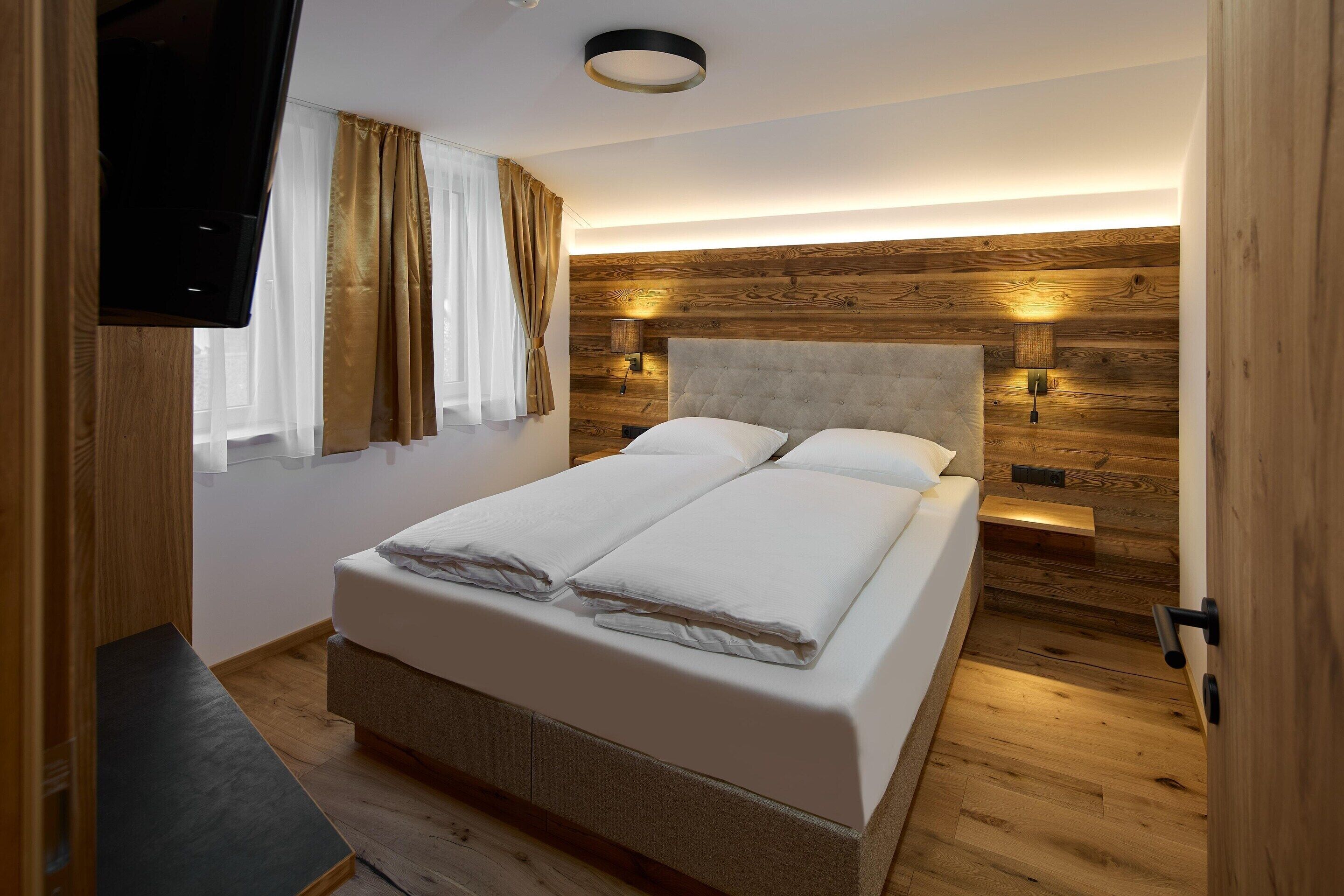 A bedroom with a bed, curtains, a mounted TV, and wooden paneling on the wall.