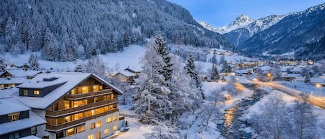 A multi-story hotel with a snow-covered landscape, a river, and mountains in the background.