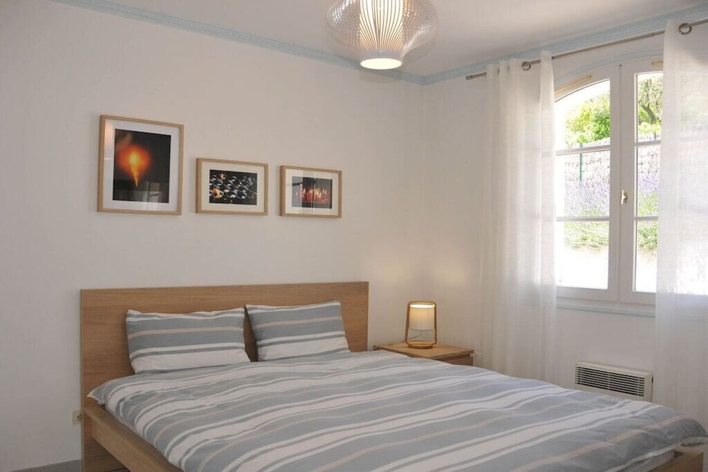 Un dormitorio con cama, mesita de noche y ventana con cortinas.