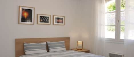 Un dormitorio con cama, mesita de noche y ventana con cortinas.