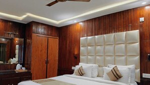 A hotel room with a large bed, wooden paneling, a ceiling fan, and a nightstand with a lamp. - The Heritage Kud (Patnitop)