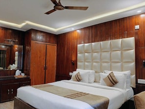 A hotel room with a large bed, wooden paneling, a ceiling fan, and a nightstand with a lamp. - The Heritage Kud (Patnitop)