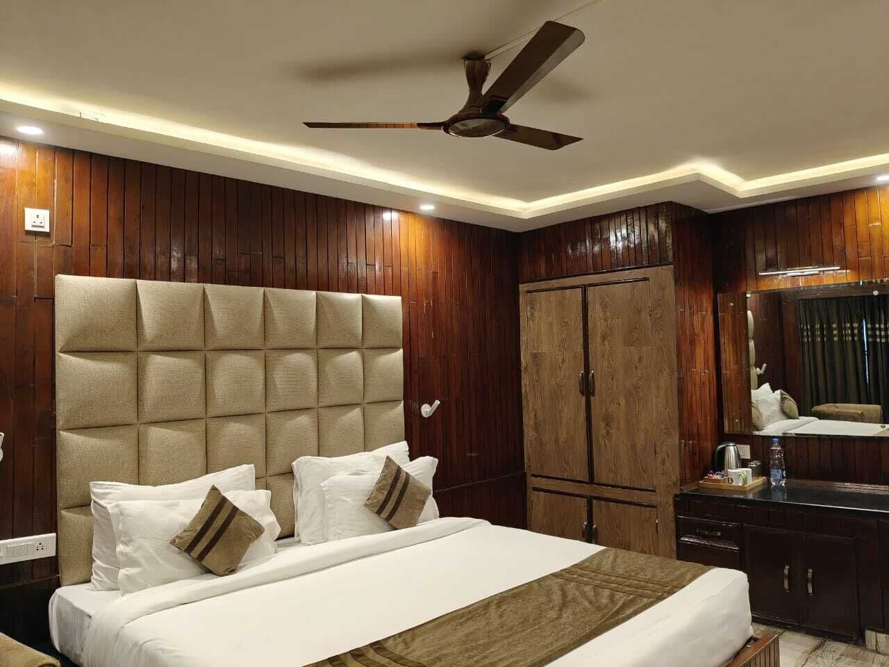 A hotel room with a large bed, wooden panel walls, a ceiling fan, and a wardrobe.