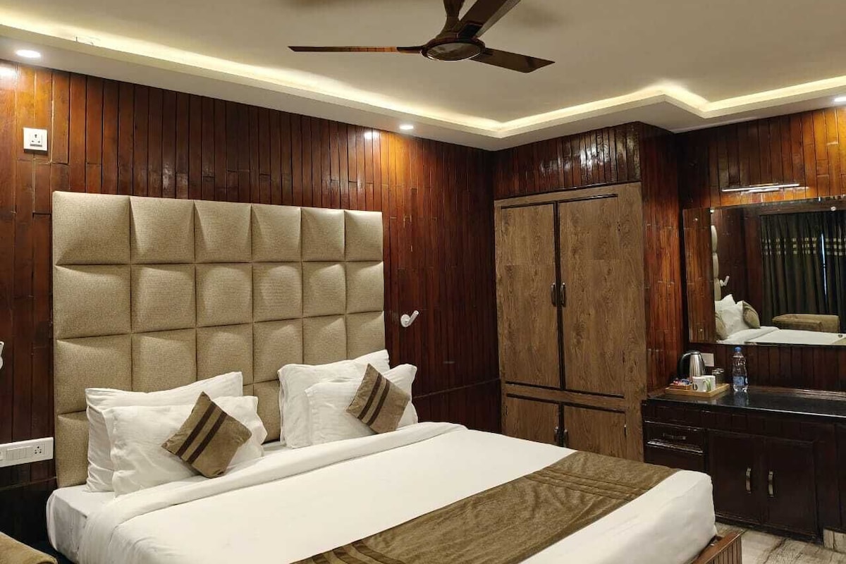 A hotel room with a large bed, wooden panel walls, a ceiling fan, and a wardrobe.