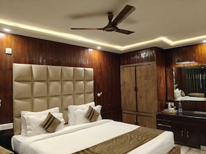A hotel room with a large bed, wooden panel walls, a ceiling fan, and a wardrobe. - The Heritage Kud (Patnitop)