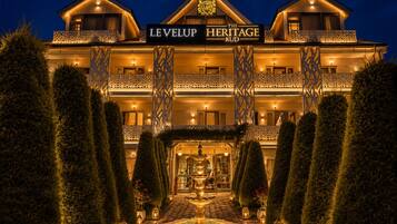 A hotel with a sign reading 'The Heritage Kud' and a well-lit entrance with a fountain.