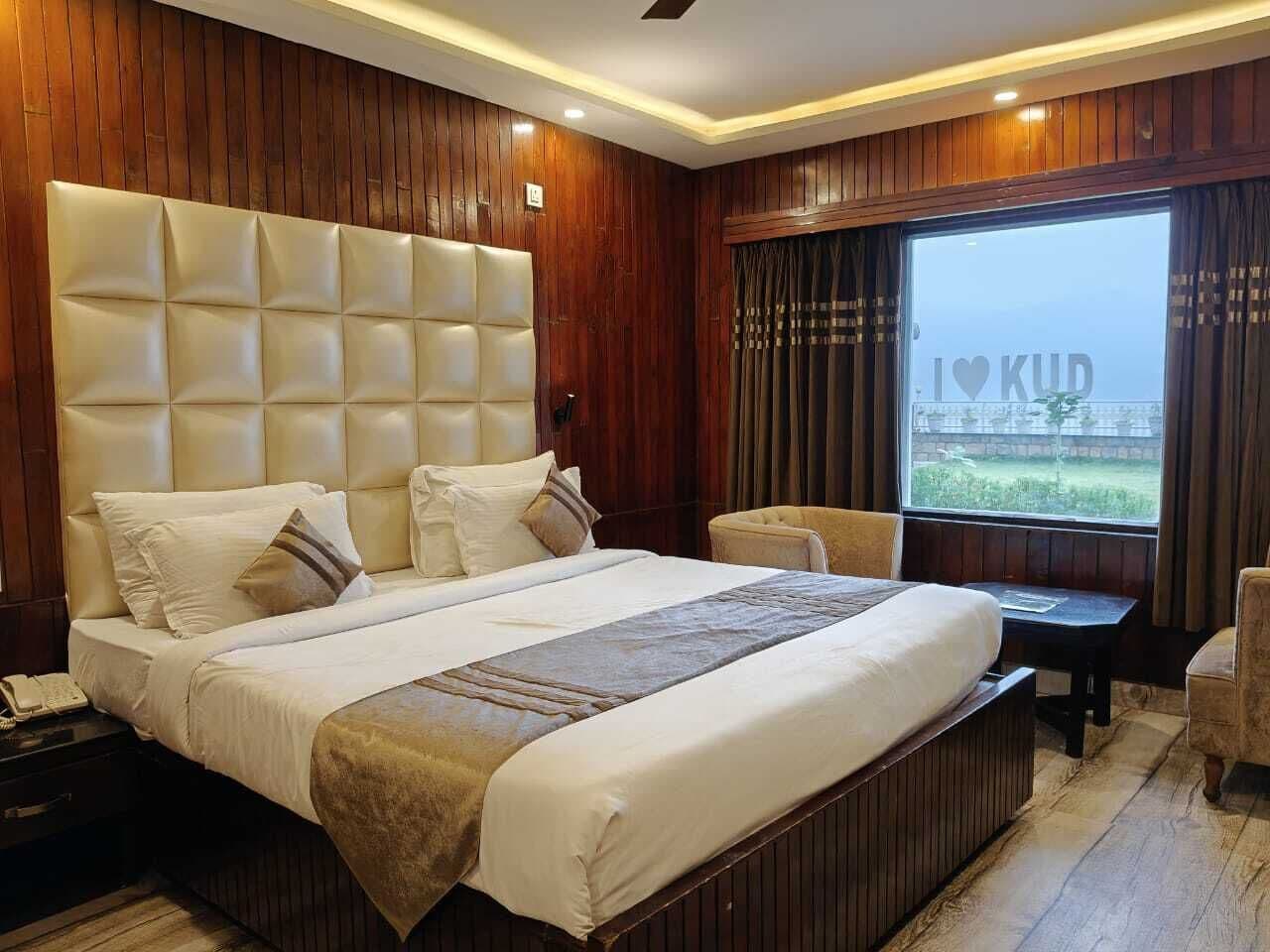 A hotel room with a large bed, a bedside table, a chair, and a window with curtains.