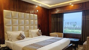 A hotel room with a large bed, a bedside table, a chair, and a window with curtains. - The Heritage Kud (Patnitop)