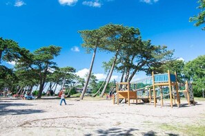 Ein Spielplatz mit Klettergerüsten und Sandboden, umgeben von Bäumen.