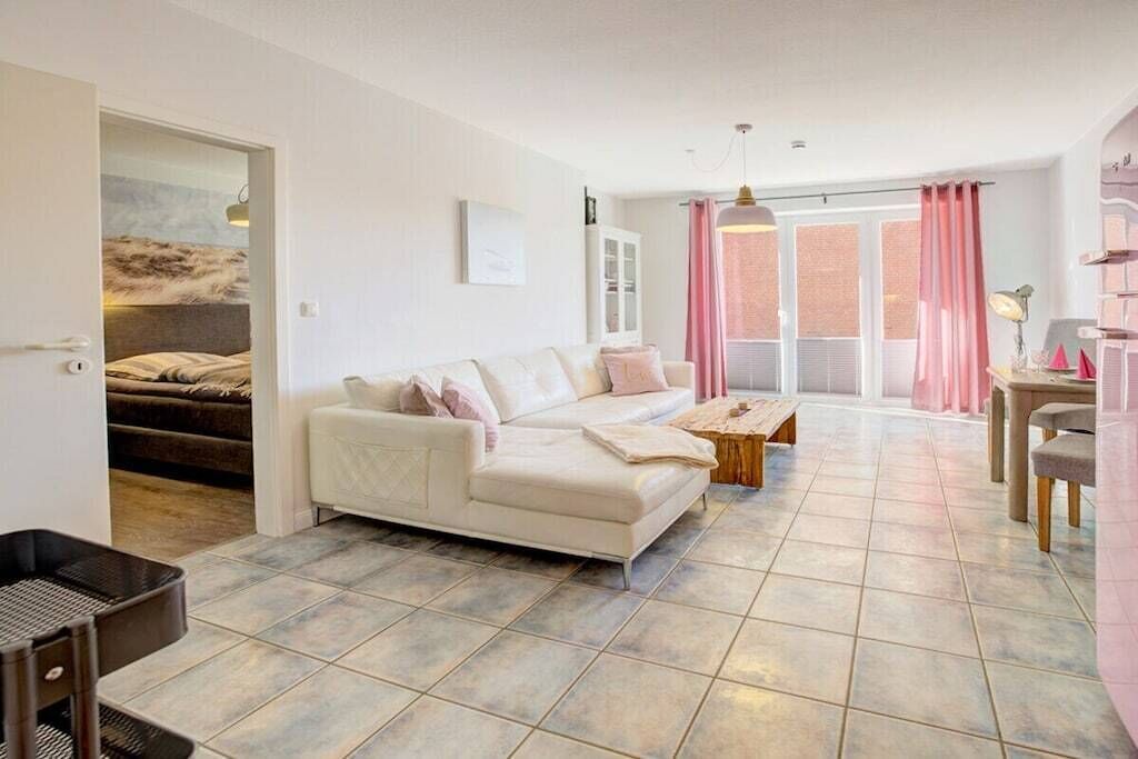 A spacious living area with a white sofa, a wooden coffee table, and a dining table with chairs. There is a sliding glass door leading to a balcony.