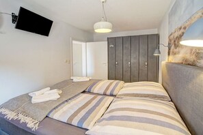 Quarto com cama, televisão de tela plana na parede, guarda-roupa e luminária.
