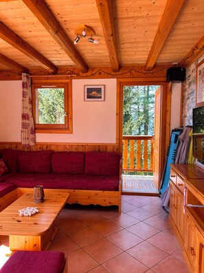 Een houten blokhut interieur met een houten plafond, een rode bank, een houten tafel en een balkon met uitzicht op bomen.