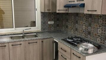 Une cuisine avec des meubles de couleur bois clair, une cuisinière à gaz, un évier et des carreaux décoratifs sur le mur derrière l’évier.
