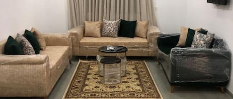 A living room with a beige sofa set, a coffee table, and a patterned rug.