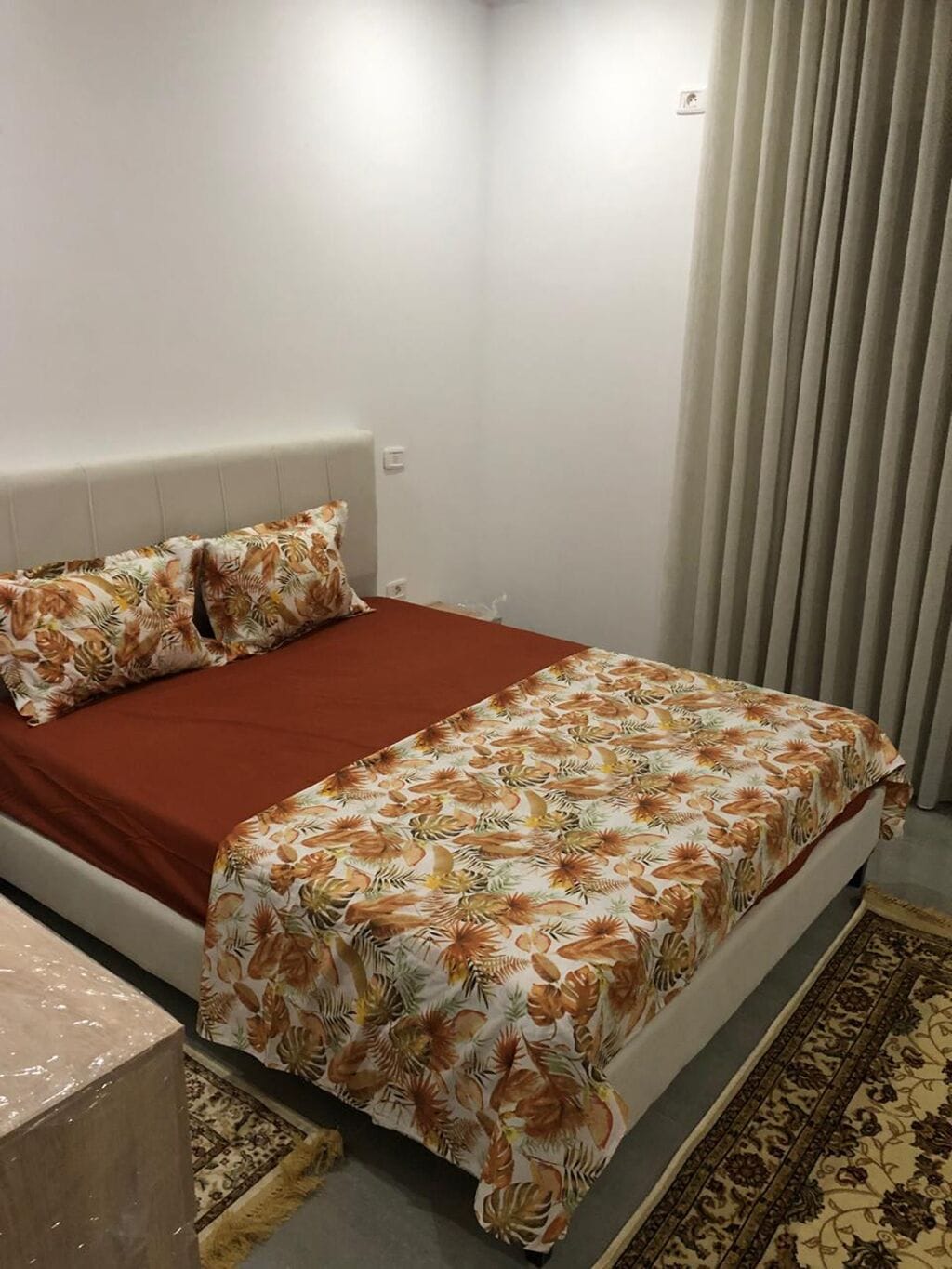 A bedroom with a bed, pillows, a nightstand, and a window with curtains.