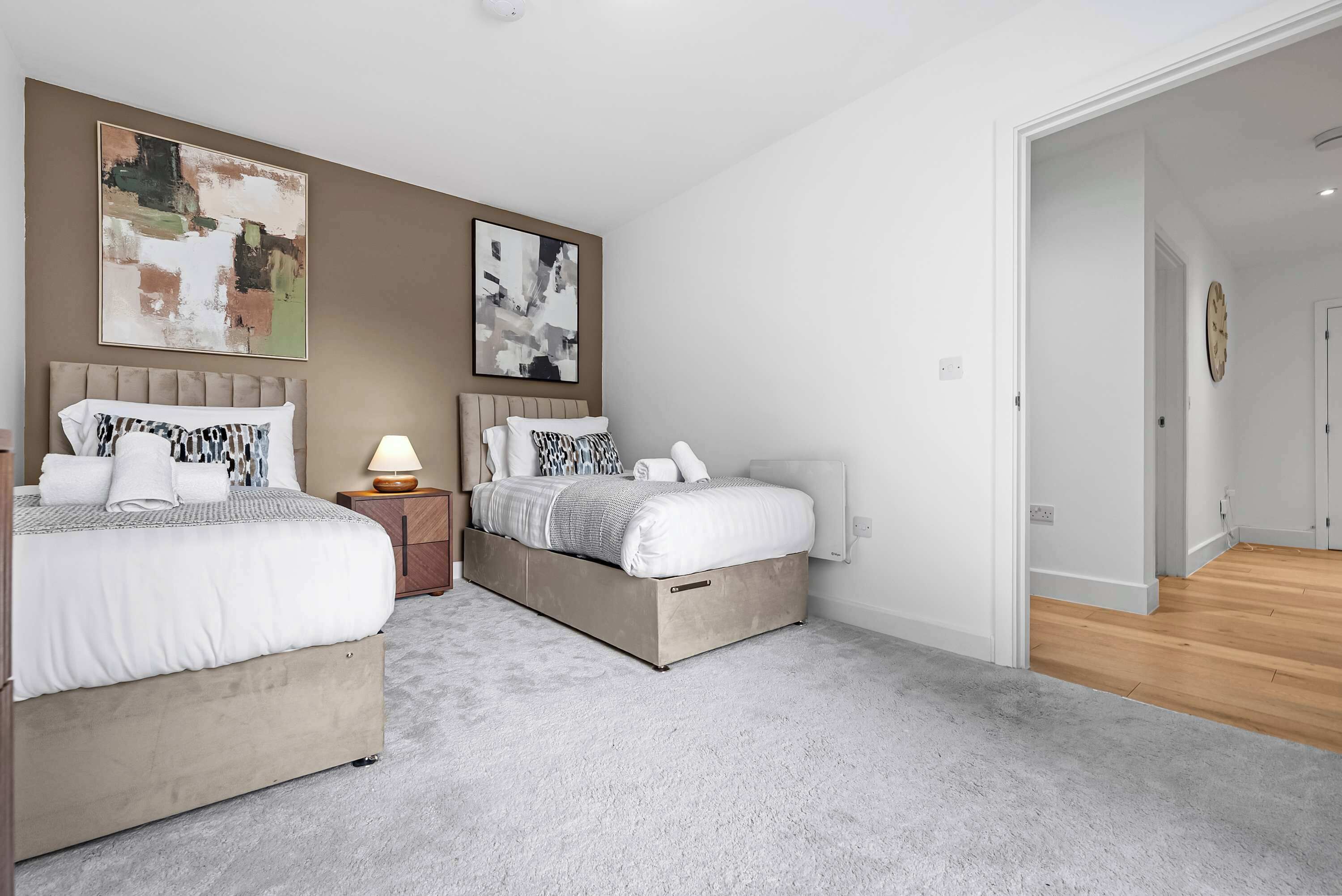 A modern bedroom with two beds, a nightstand, and abstract art on the walls.