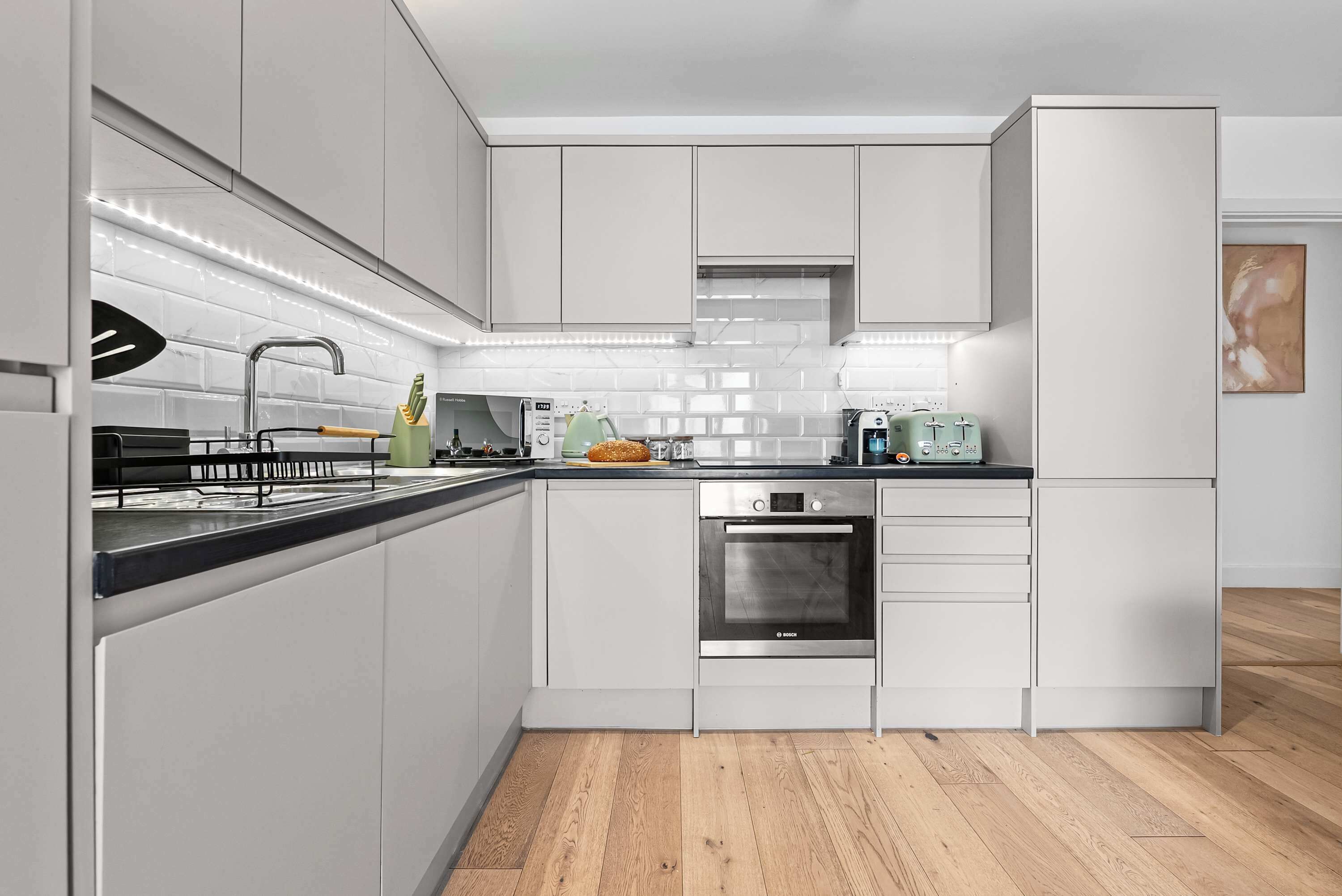 A modern kitchen with white cabinetry, a Bosch oven, and a coffee machine.