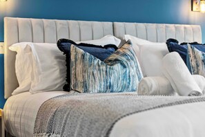 Ein Bett mit einem gesteppten Kopfteil, Kissen in Weiß und Blau mit Muster, und einer grauen Decke.