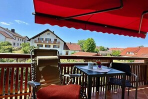 Un balcón con una mesa, sillas y un toldo rojo.