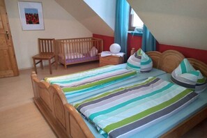A bedroom with a sloped ceiling, a wooden crib, a wooden chair, a bedside table with a lamp, and a bed with striped bedding. - Cherry Orchard at Haus Bayer (Pottenstein)