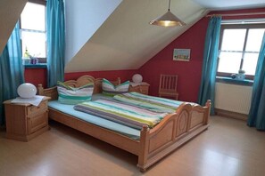 Un dormitorio con techo inclinado, una cama con ropa de cama a rayas, una mesita de noche con lámpara y una ventana con cortinas.