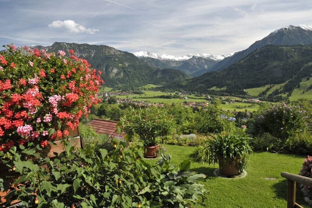 Un jardin où l’on trouve une grande variété de plantes et de fleurs, une clôture en bois et, en arrière-plan, un paysage montagneux.