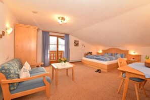 Ein gemütliches Zimmer mit einem Bett, einer Couch, einem kleinen Tisch mit einer Vase und einem Sessel.