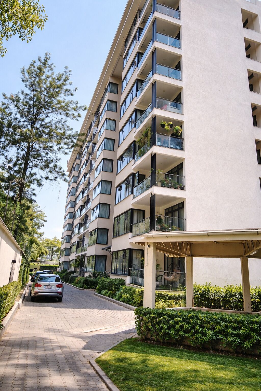 A multi-story residential building with balconies, a covered entrance, and a paved driveway.