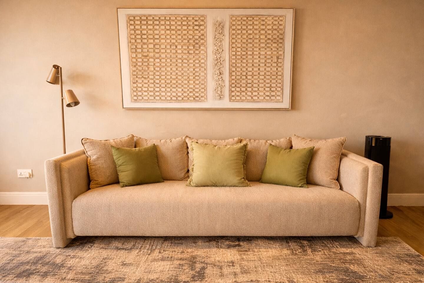 A beige sofa with green cushions, a patterned rug, and a framed artwork above.