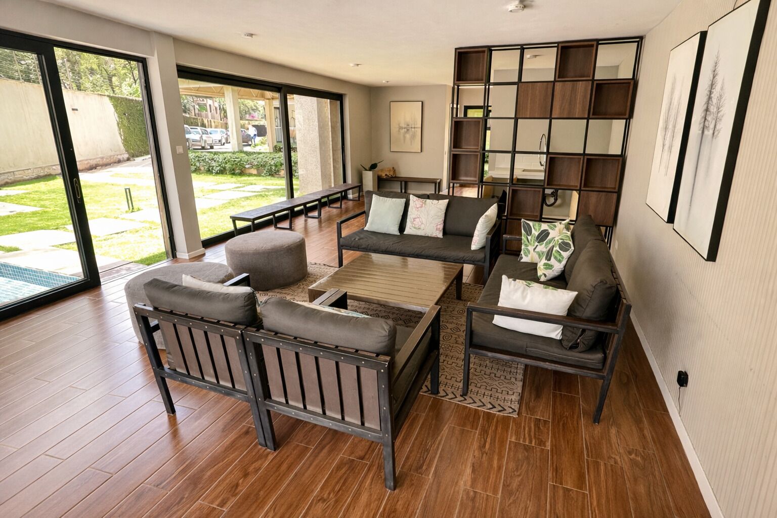 A spacious living room with a sofa set, a coffee table, and a large window offering a view of the outdoors.