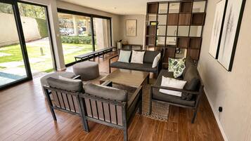 A spacious living room with a sofa set, a coffee table, and a large window offering a view of the outdoors.