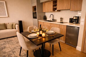 Uma área de refeições com mesa posta para quatro pessoas, um sofá e uma cozinha ao fundo.