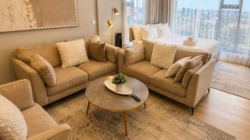 Habitación de hotel moderna con una cama grande, dos sofás, una mesa de centro y vistas a la ciudad.