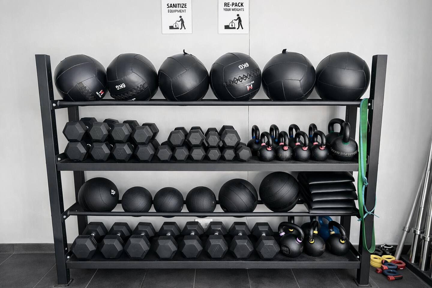 Un gimnasio con equipo, incluyendo mancuernas, kettlebells y balones medicinales sobre estanterías.