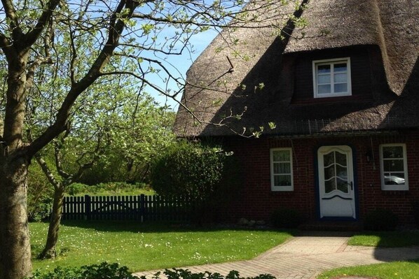 Een traditioneel huis met bakstenen muren, een rieten dak, een voordeur en een klein raam.